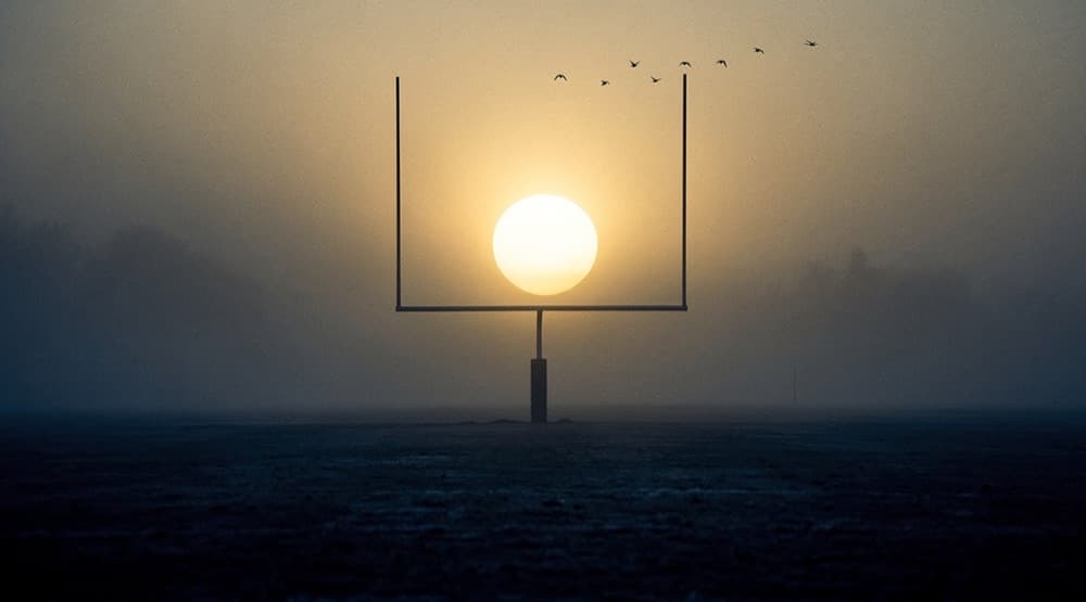 A goalpost silhouetted in fog against the sunrise